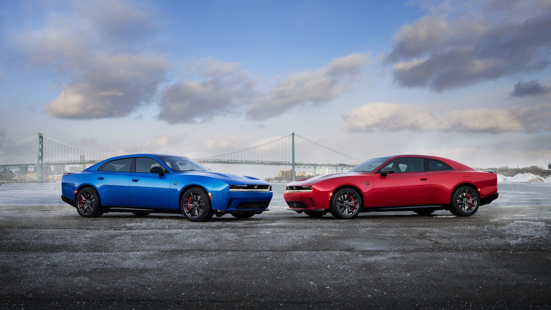Blue and red 2026 Dodge Charger models parked side by side beside a suspension bridge.