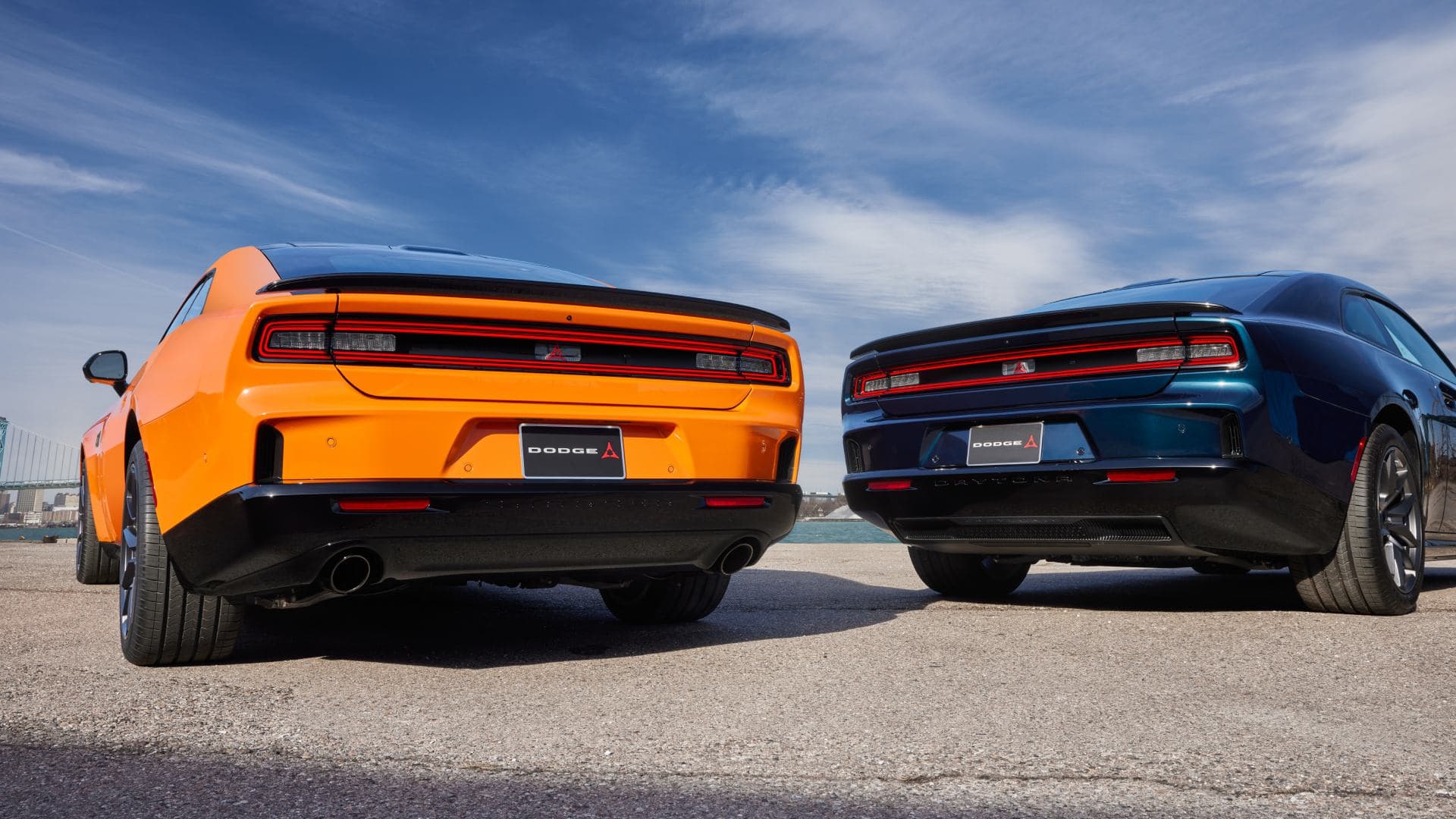 Rear view of an orange gas-powered 2026 Dodge Charger with dual exhaust beside a blue Charger.