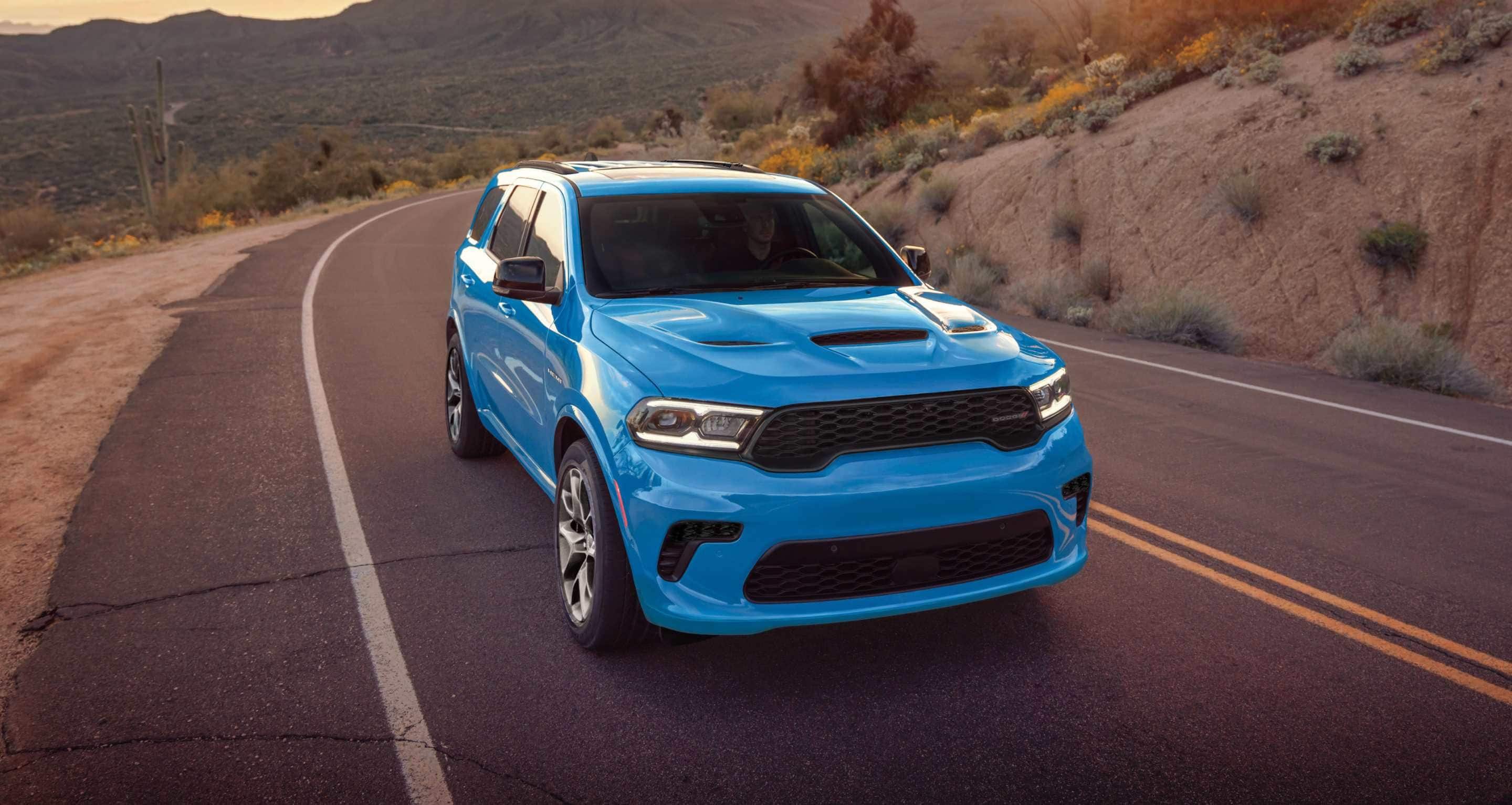 A blue 2026 Dodge Durango GT HEMI traveling down a winding highway in the mountains.