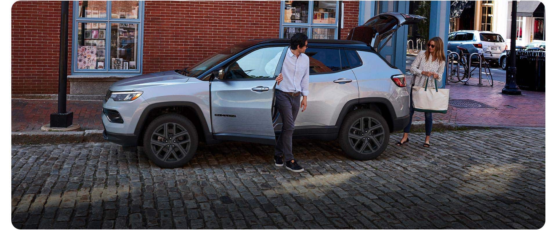 Silver 2026 Jeep Compass parked on a cobblestone street with its liftgate open.