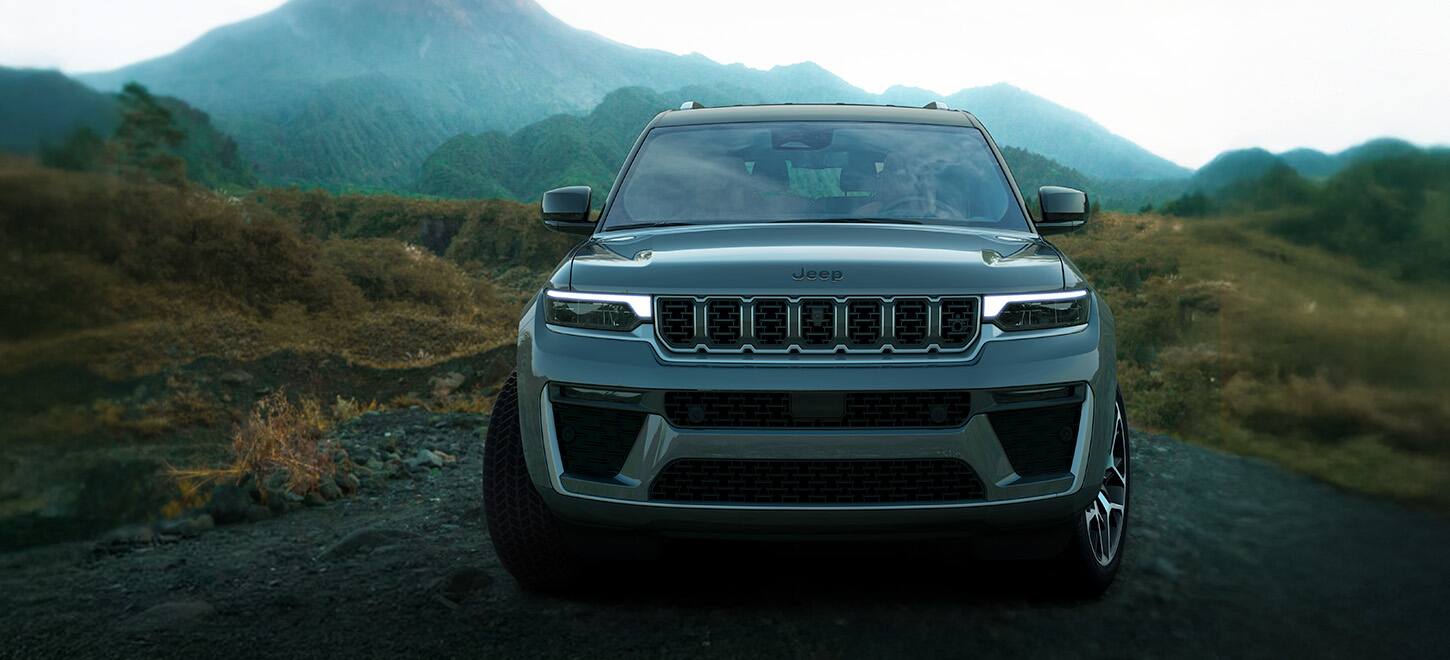 A head-on angle of a gray 2026 Jeep Grand Cherokee, traveling on a trail off-road in the mountains.