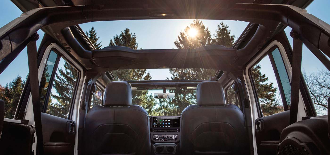 The interior of a 2026 Jeep Wrangler four-door, focusing on the spacious view from the open sunroof, as shot from the rear seat.