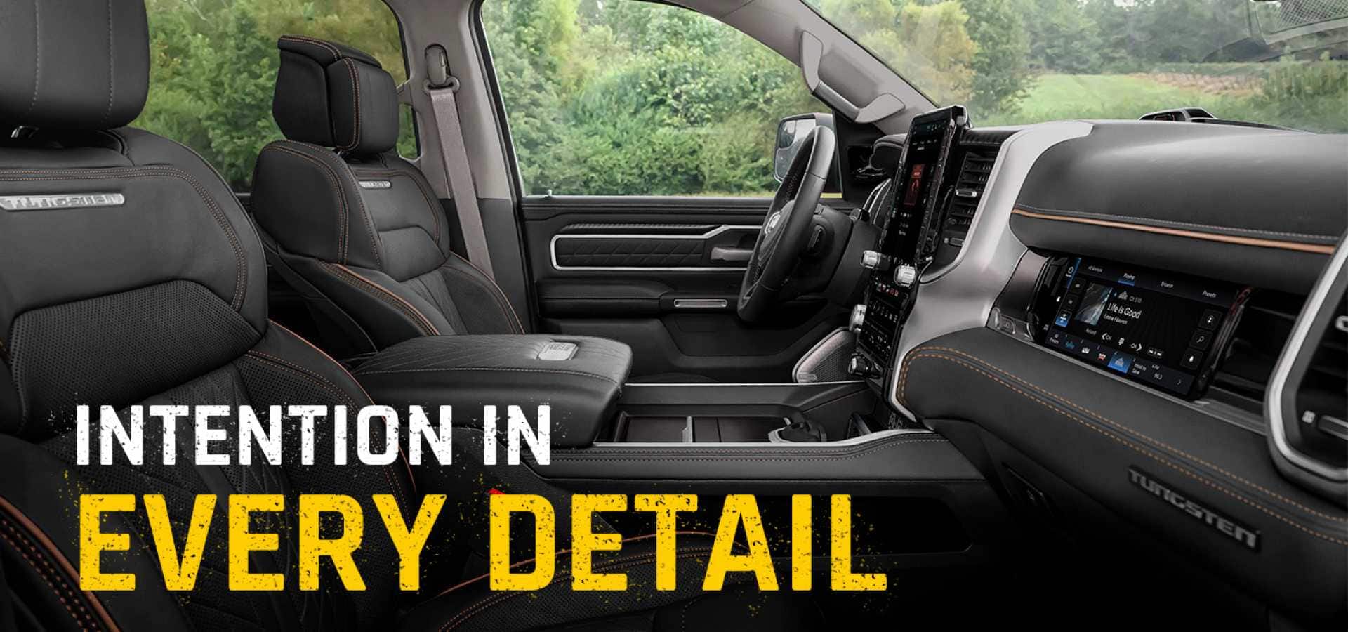 The front row of a 2027 Ram 1500 Tungsten 4x4 Crew Cab shot from the passenger side, with dark gray bucket seats and a Front Passenger Interactive Touchscreen Display. Intention In Every Detail.