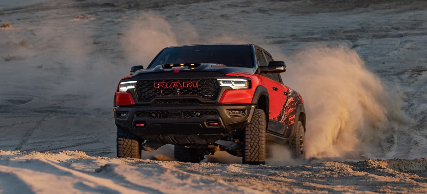 A red 2027 Ram 1500 SRT Bloodshot Night Edition with black hood and roof, traveling through the desert, off-road.