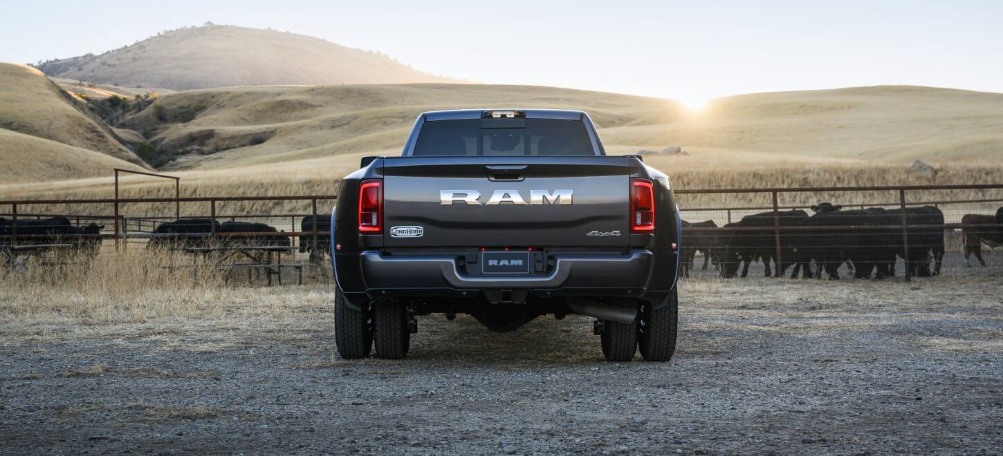 The rear angle of a black 2027 Ram 3500 Heavy Duty Limited Longhorn 4x4 Crew Cab pickup truck parked at a cattle ranch.